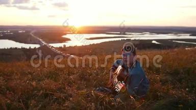 戴着圆眼镜的男孩在日落时分的田野里弹吉他，仰望天空